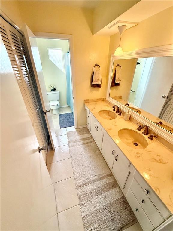 full bathroom featuring a sink, toilet, double vanity, and tile patterned flooring