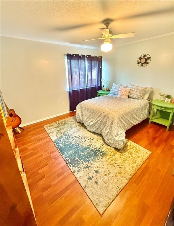 bedroom with ornamental molding, a ceiling fan, a textured ceiling, wood finished floors, and baseboards