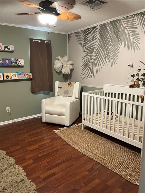 bedroom featuring visible vents, a crib, wood finished floors, crown molding, and baseboards