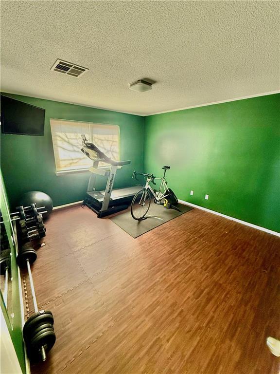 exercise area with wood finished floors, visible vents, and baseboards