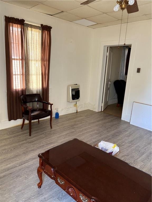 sitting room featuring baseboards, ceiling fan, a drop ceiling, wood finished floors, and heating unit