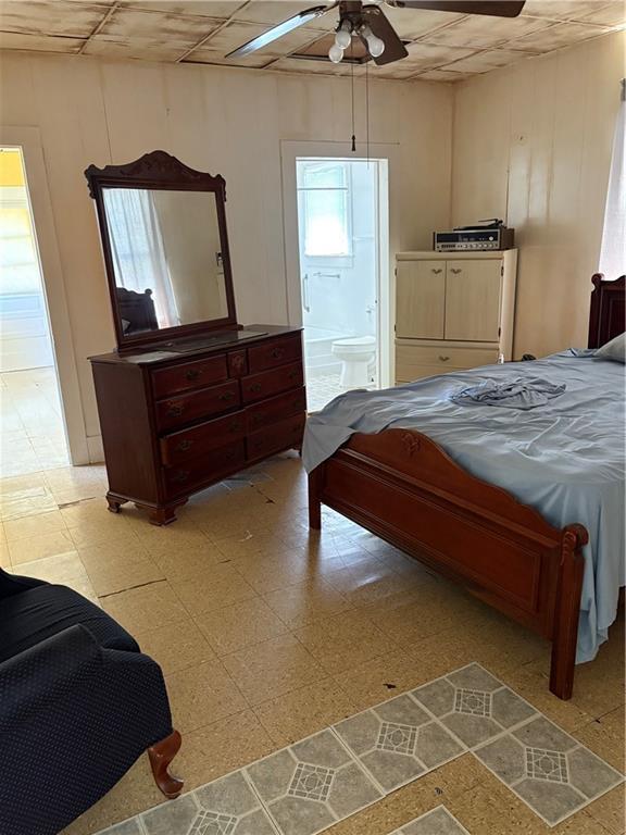 bedroom featuring a drop ceiling, light floors, ensuite bath, and ceiling fan