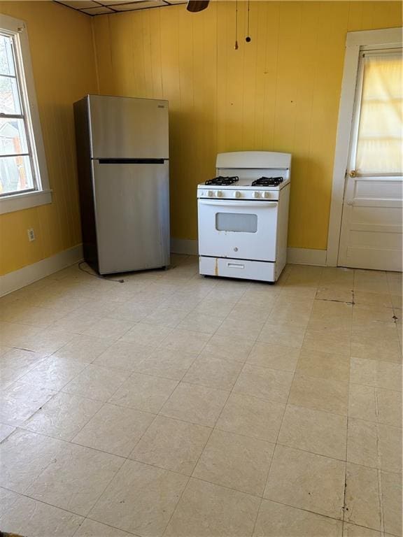 kitchen featuring gas range gas stove, baseboards, freestanding refrigerator, and wood walls