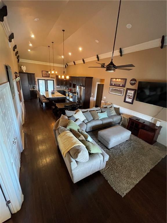 living area with dark wood finished floors, ceiling fan with notable chandelier, crown molding, and lofted ceiling