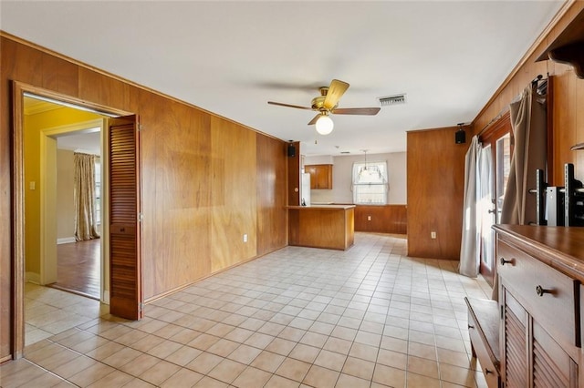 empty room featuring light tile patterned floors, visible vents, wooden walls, and ceiling fan