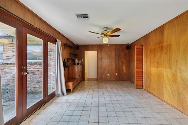 spare room with wooden walls, visible vents, a ceiling fan, and light tile patterned flooring