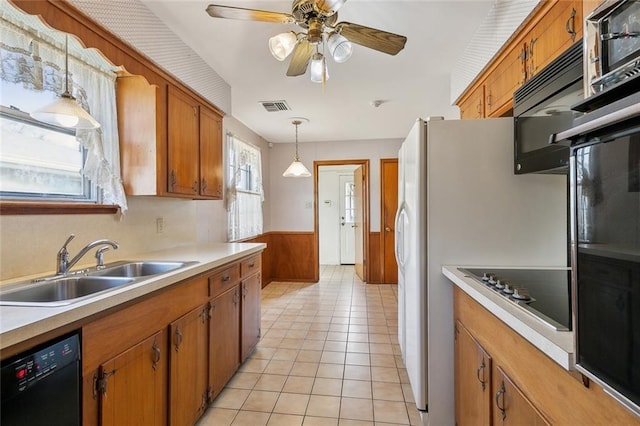 kitchen featuring visible vents, wainscoting, brown cabinetry, black appliances, and a sink