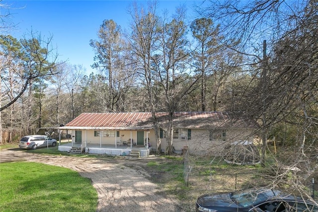 ranch-style house with a porch, a wooded view, a front lawn, and metal roof