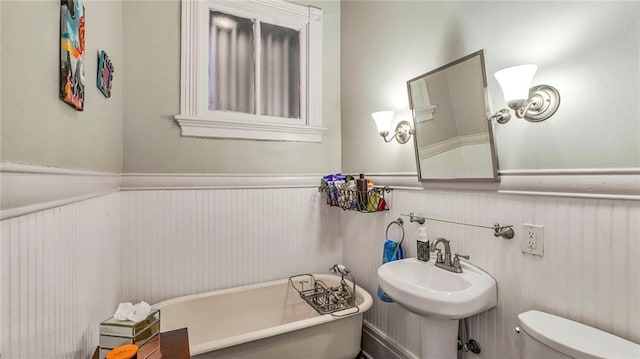 bathroom with a sink, a soaking tub, toilet, and wainscoting