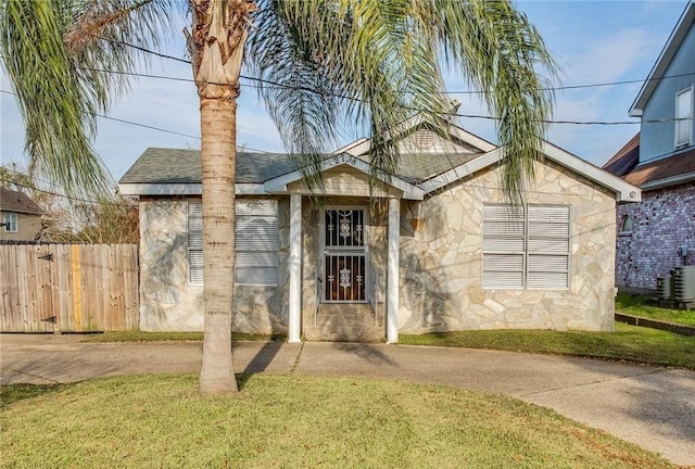 ranch-style home featuring a front yard, fence, stone siding, and a shingled roof