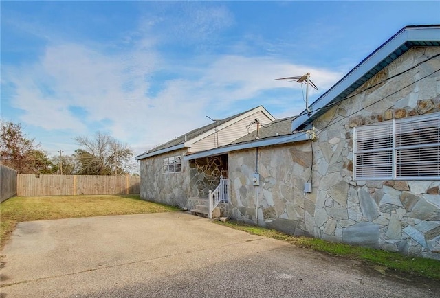 view of property exterior with a yard, stone siding, a patio, and fence