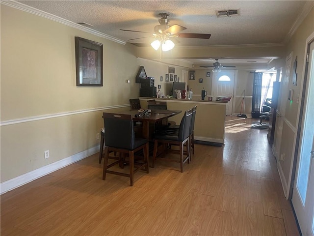 dining room featuring a ceiling fan, wood finished floors, visible vents, a textured ceiling, and crown molding