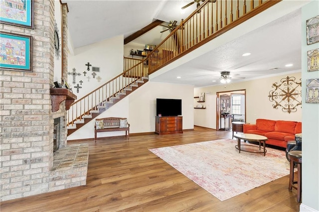 living room featuring stairway, wood finished floors, baseboards, ceiling fan, and a towering ceiling