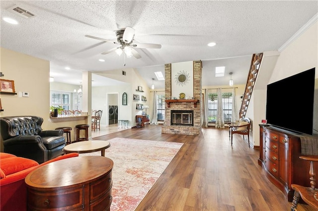 living room featuring visible vents, a fireplace, wood finished floors, a textured ceiling, and a ceiling fan