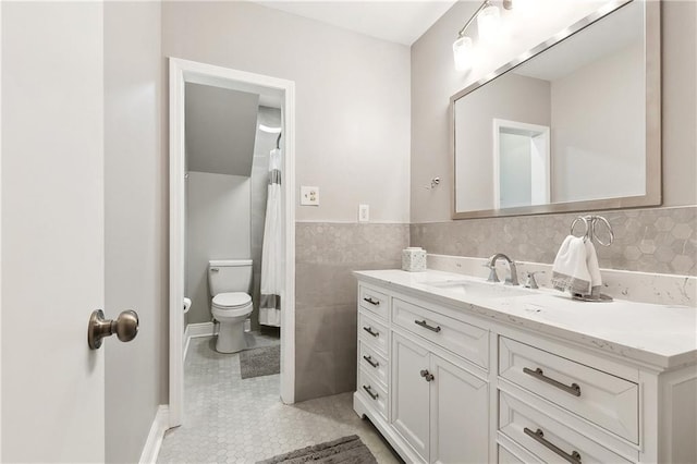 full bath with tile patterned floors, a wainscoted wall, toilet, tile walls, and vanity