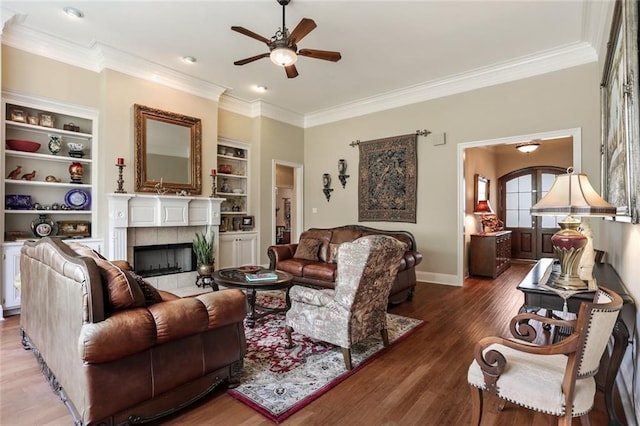 living area with crown molding, wood finished floors, ceiling fan, a tiled fireplace, and baseboards