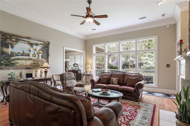 living room with crown molding, a ceiling fan, light wood-style floors, baseboards, and visible vents