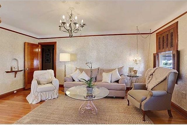 living area with baseboards, wood finished floors, a chandelier, and crown molding