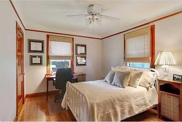 bedroom featuring ceiling fan, baseboards, wood finished floors, and ornamental molding