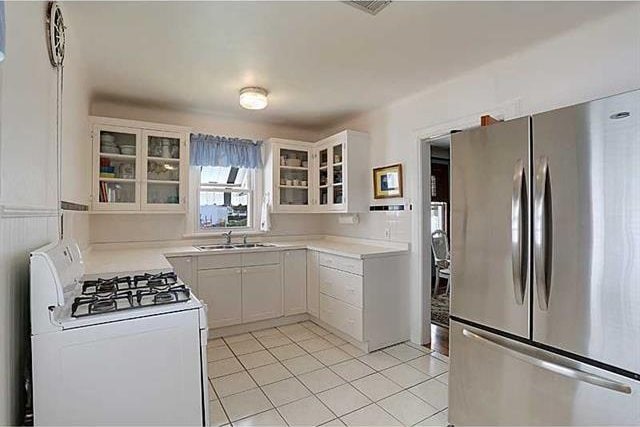 kitchen with light tile patterned flooring, light countertops, freestanding refrigerator, and gas range gas stove