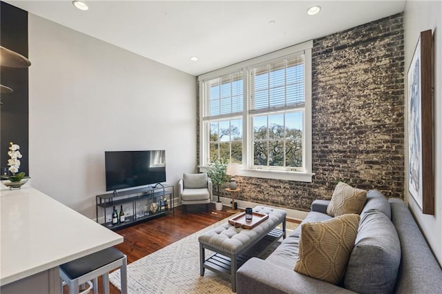 living room featuring recessed lighting, baseboards, wood finished floors, and brick wall