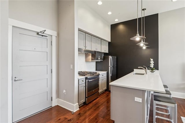 kitchen with a breakfast bar, dark wood finished floors, a sink, stainless steel appliances, and under cabinet range hood