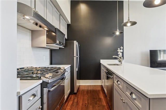 kitchen with dark wood finished floors, a sink, light countertops, under cabinet range hood, and appliances with stainless steel finishes