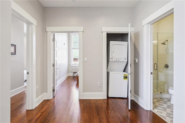 interior space featuring stacked washer / drying machine, baseboards, wood finished floors, and laundry area