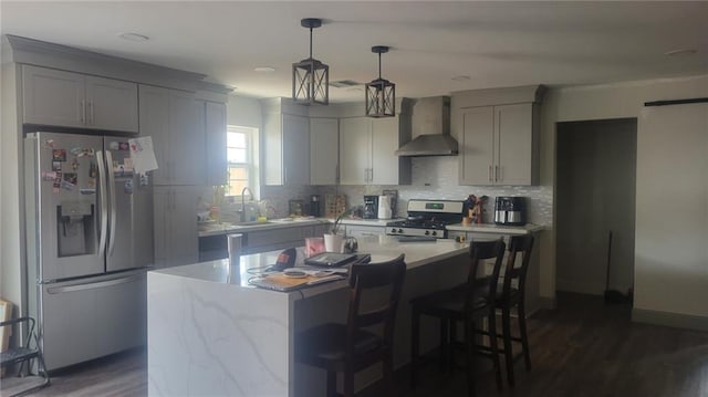 kitchen with a kitchen island, backsplash, dark wood-style floors, appliances with stainless steel finishes, and wall chimney range hood