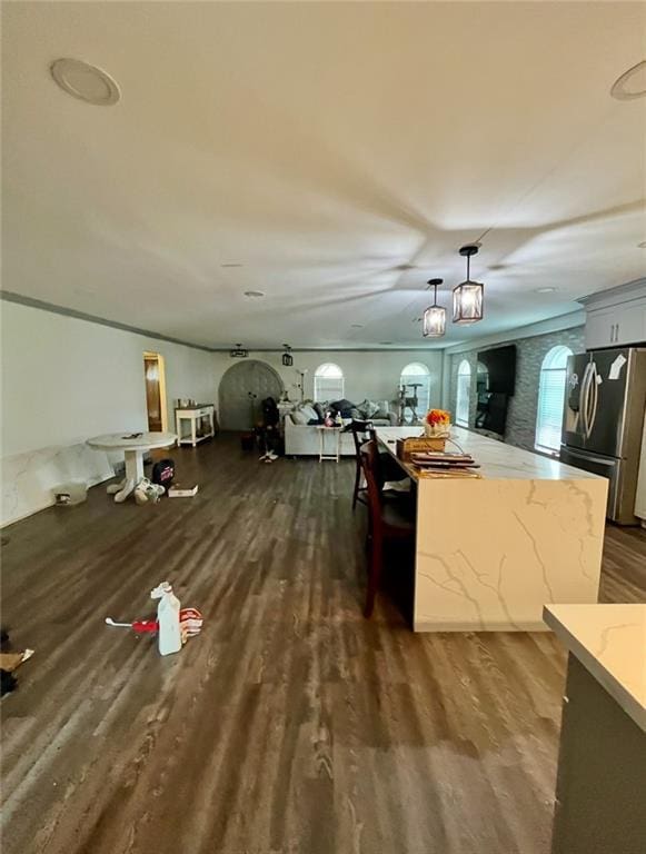 kitchen featuring pendant lighting, dark wood-style floors, a center island, stainless steel fridge with ice dispenser, and light stone countertops