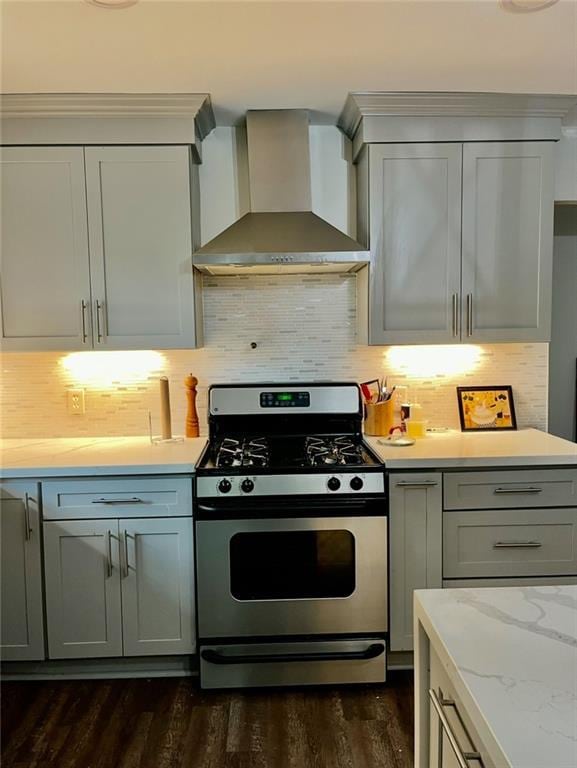 kitchen with gray cabinetry, dark wood-type flooring, stainless steel gas stove, wall chimney range hood, and tasteful backsplash