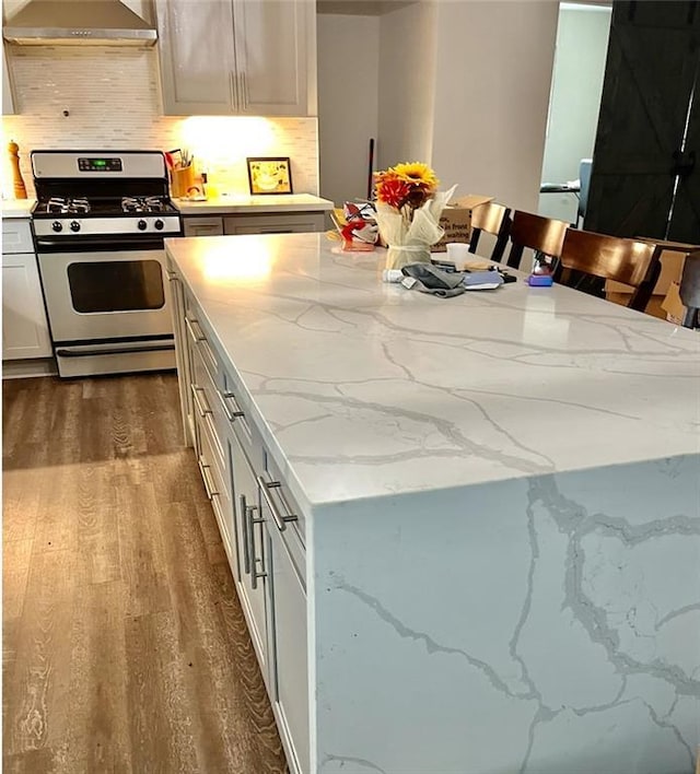 kitchen with dark wood-type flooring, a kitchen island, wall chimney exhaust hood, decorative backsplash, and gas range