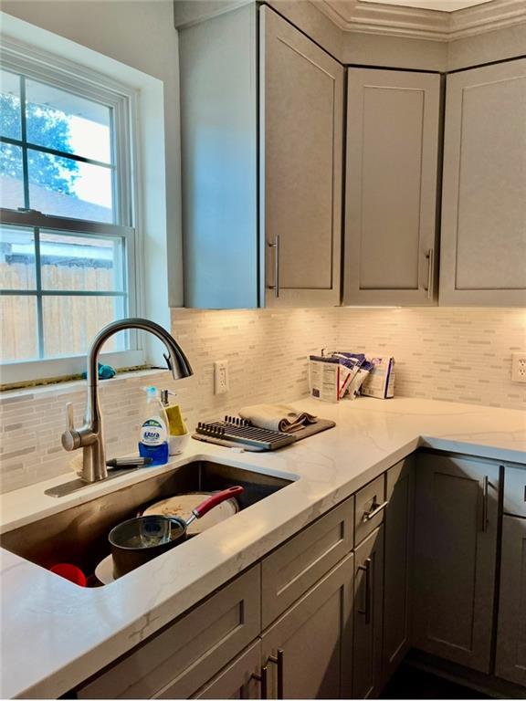 kitchen featuring a sink, light stone counters, tasteful backsplash, and gray cabinetry