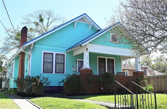 view of front of property featuring a porch, fence, a front yard, and a chimney