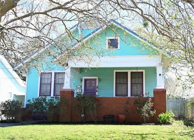 view of front of property featuring brick siding, covered porch, a front yard, and fence