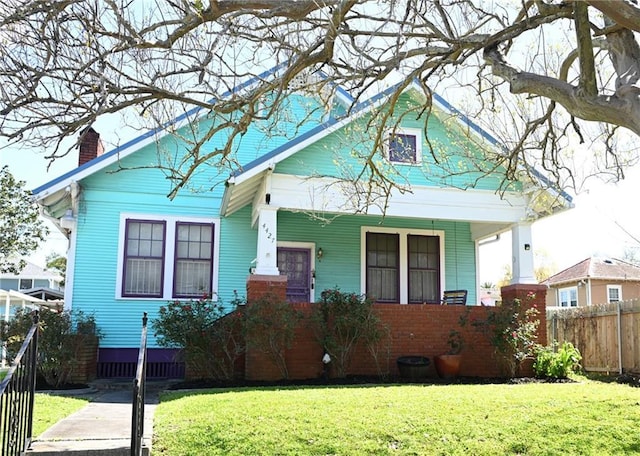 view of front of house featuring covered porch, a chimney, a front lawn, and fence