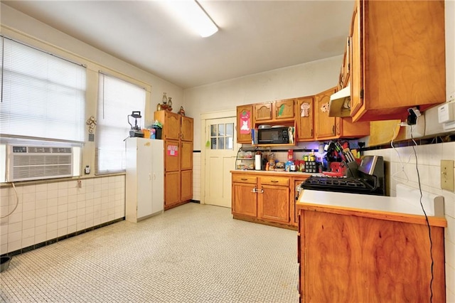 kitchen with black appliances, a healthy amount of sunlight, brown cabinetry, and light countertops