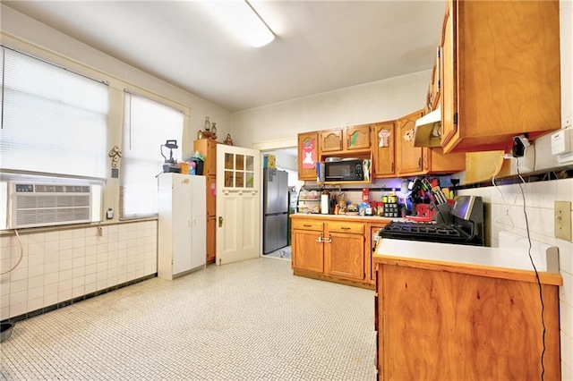 kitchen featuring freestanding refrigerator, gas stove, brown cabinetry, light countertops, and black microwave