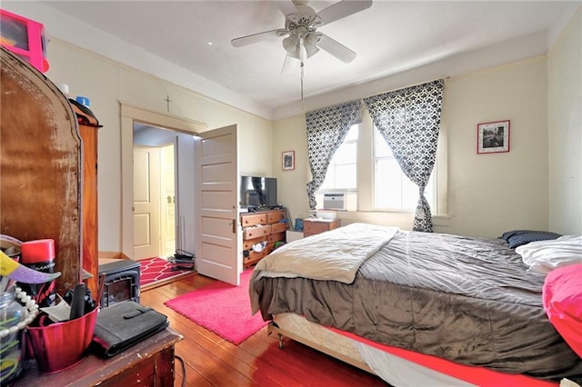 bedroom with ceiling fan, a wood stove, and hardwood / wood-style flooring