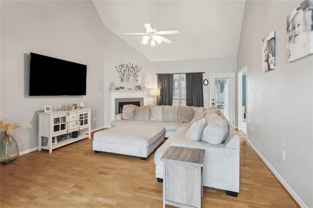 living area featuring light wood-style flooring, a fireplace, baseboards, and ceiling fan