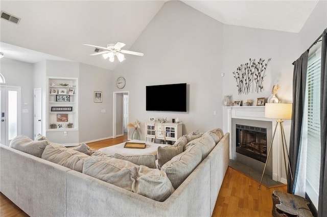 living area with built in features, a ceiling fan, visible vents, a fireplace, and light wood-style floors