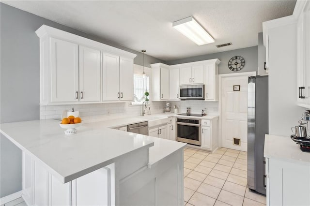 kitchen featuring visible vents, a peninsula, a sink, stainless steel appliances, and light countertops