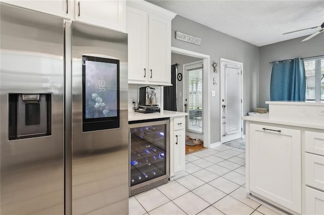 kitchen with light tile patterned floors, beverage cooler, light countertops, stainless steel refrigerator with ice dispenser, and white cabinetry