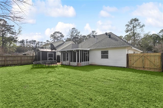 rear view of property featuring a trampoline, a fenced backyard, a yard, and a sunroom