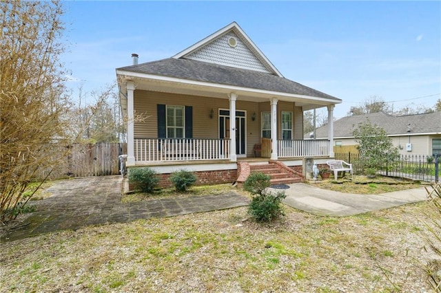 view of front facade with fence, covered porch, and roof with shingles