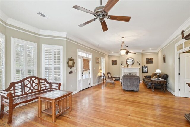 living room featuring visible vents, ornamental molding, light wood-style flooring, baseboards, and ceiling fan