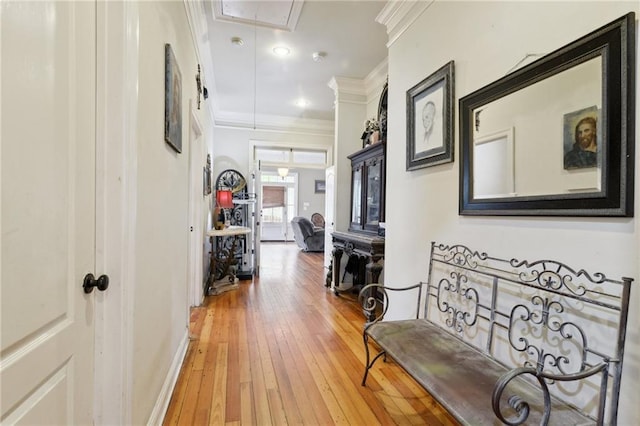 hall featuring light wood-style flooring, baseboards, attic access, and ornamental molding
