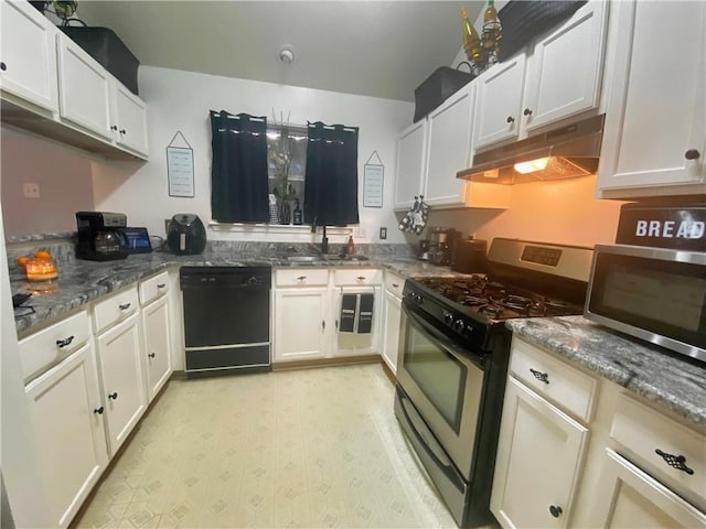 kitchen with under cabinet range hood, dark stone counters, appliances with stainless steel finishes, and a sink