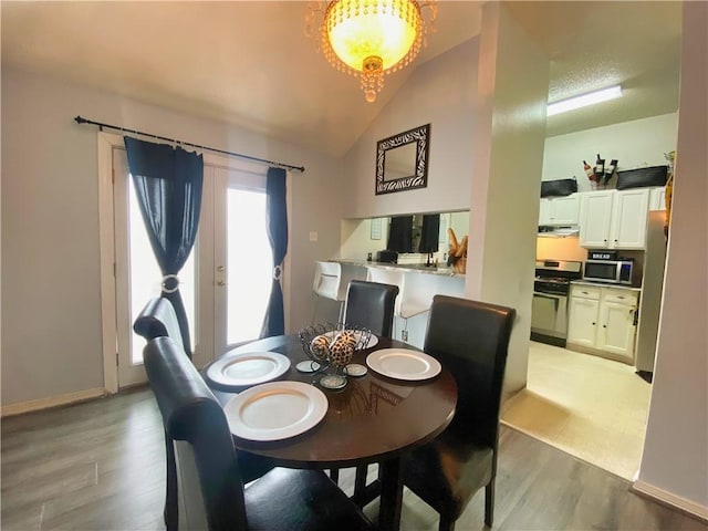 dining room featuring a notable chandelier, baseboards, light wood-style floors, and lofted ceiling