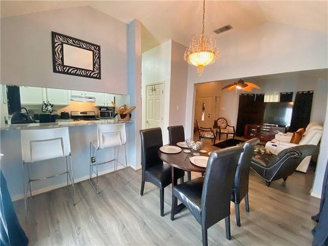 dining area with light wood-type flooring, ceiling fan with notable chandelier, visible vents, and high vaulted ceiling